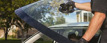 Technician holding new windshield, about to install it in a car