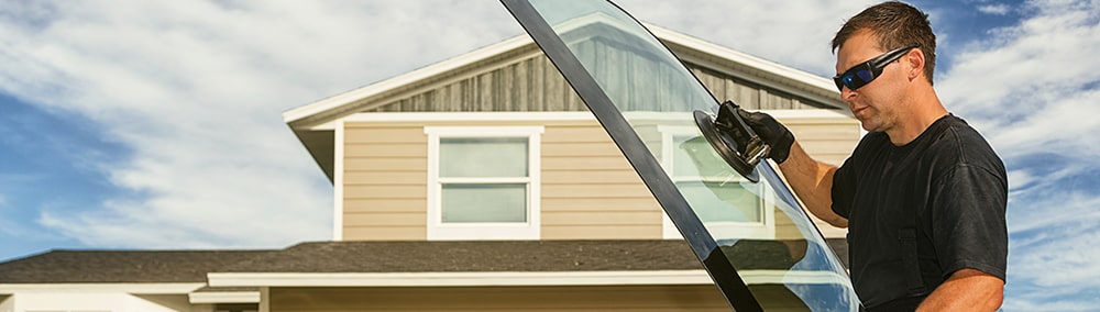 Man holding new windshield in front of house