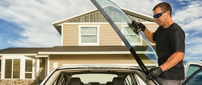 Man holding new windshield in front of house